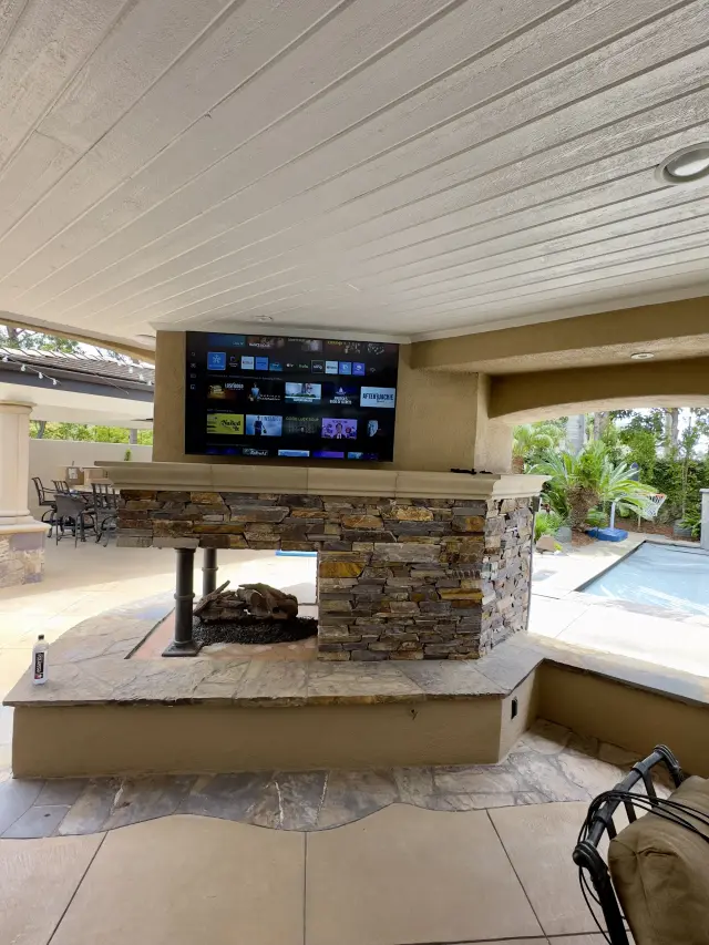 Outdoor patio television installation above fireplace entertainment area